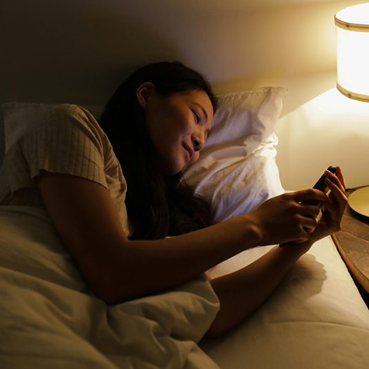 Mujer revisando su celular en el borde de la cama.